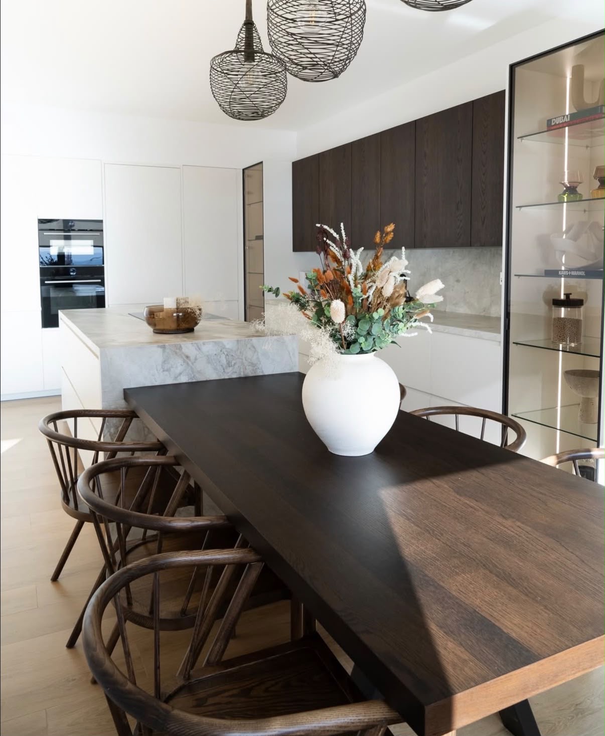 Open-plan kitchen and dining space with dark oak cabinetry, marble island and statement woven pendants