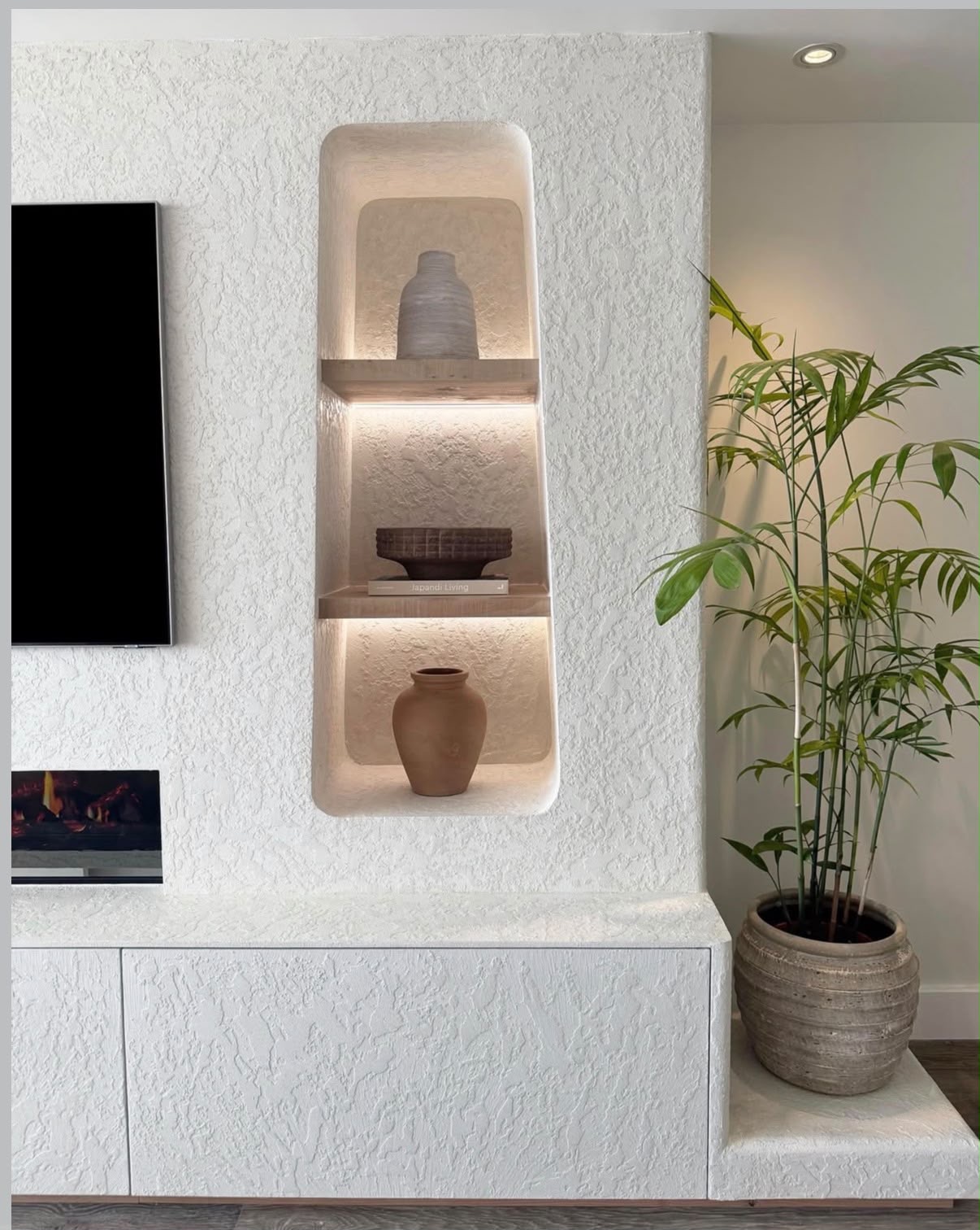 Textured plaster media wall with curved backlit niche, oak shelves and integrated fireplace