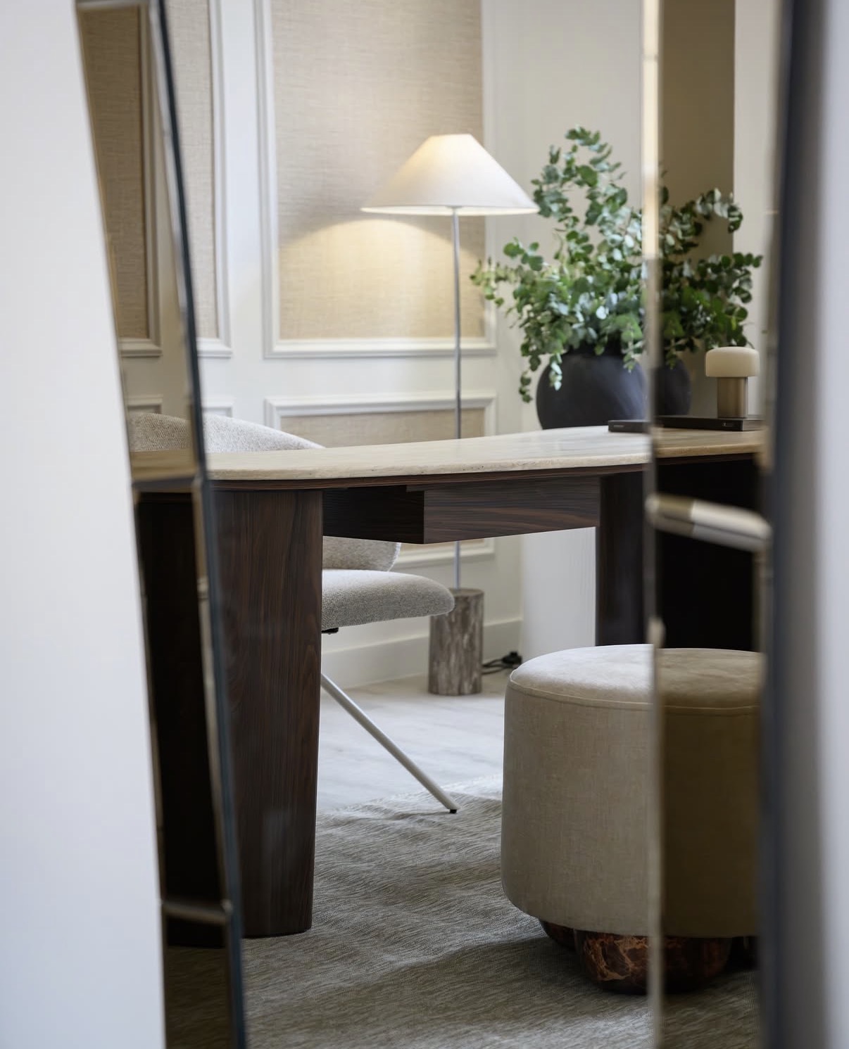 Detail of the studio desk and seating, reflected in a mirror with soft lamplight and greenery