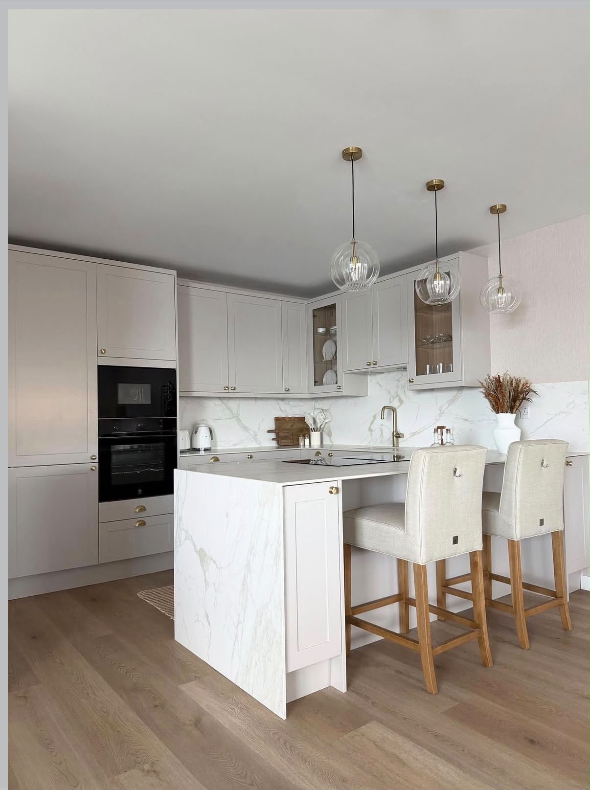 Soft greige shaker kitchen with a marble peninsula, ribbed glass globe pendants and linen bar stools