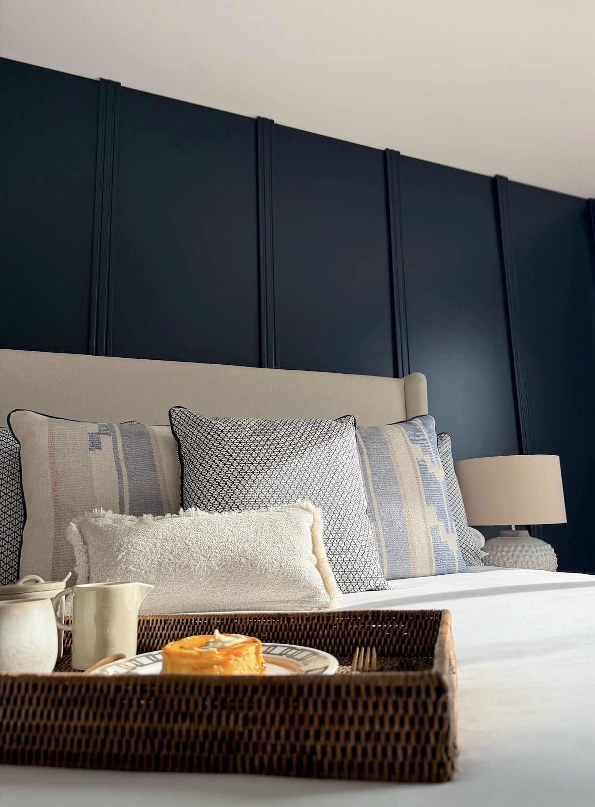 Bedroom with deep navy panelled feature wall, upholstered bed and breakfast tray styling