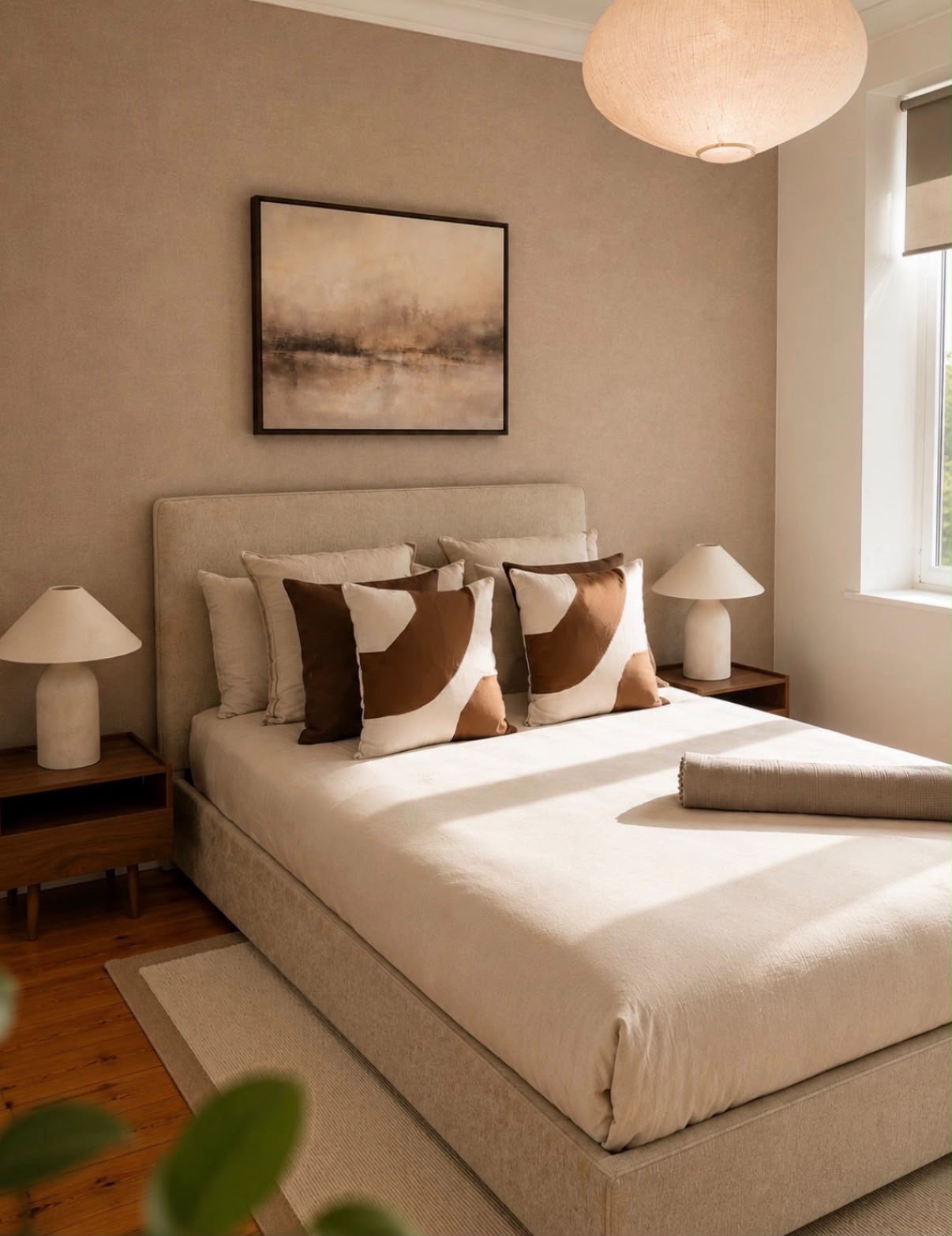 Sunlit bedroom with warm taupe textured walls, linen bed, walnut bedside tables and a rice paper pendant