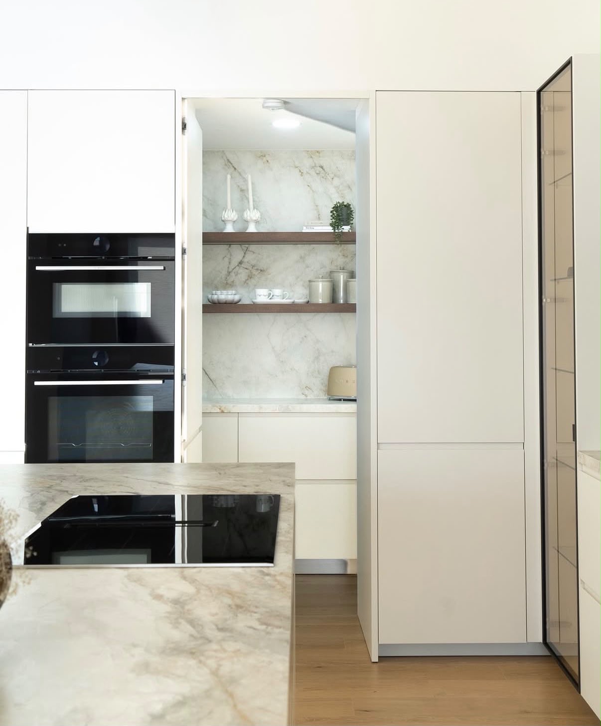 Bespoke floor-to-ceiling ivory cabinetry with concealed doors revealing a marble-lined coffee station with walnut shelving
