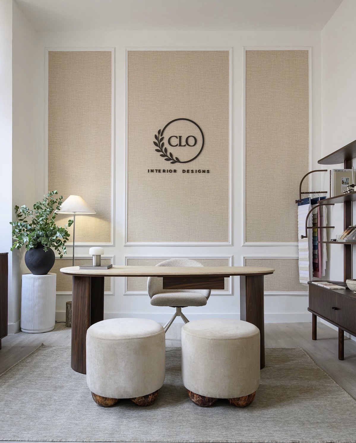 The Clo Interior Designs studio — a light-filled consultation space with a walnut desk, ivory stools, and the Clo logo on a textured wall