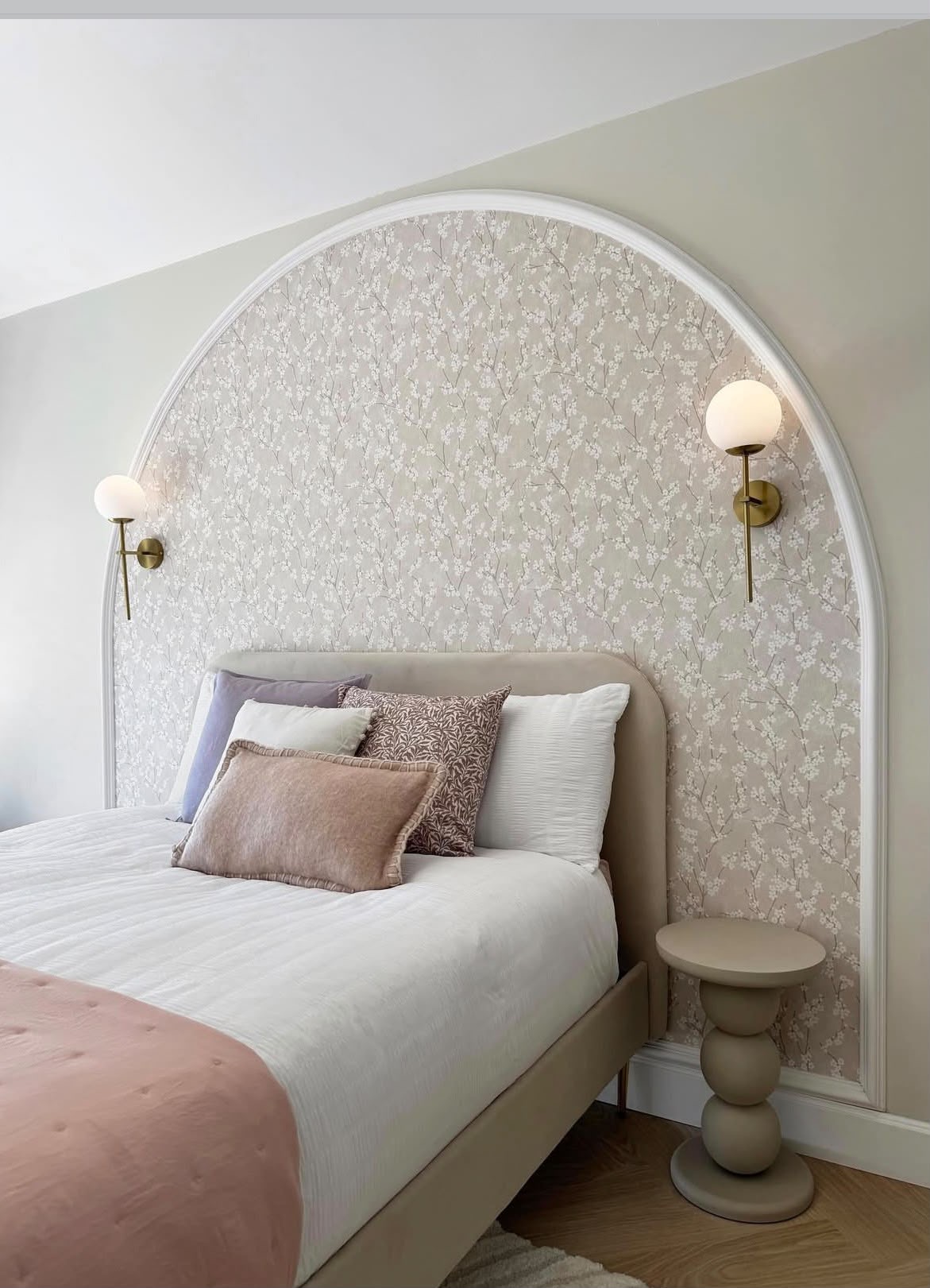 Child's bedroom with arched wallpapered alcove, upholstered bed and brass globe wall lights