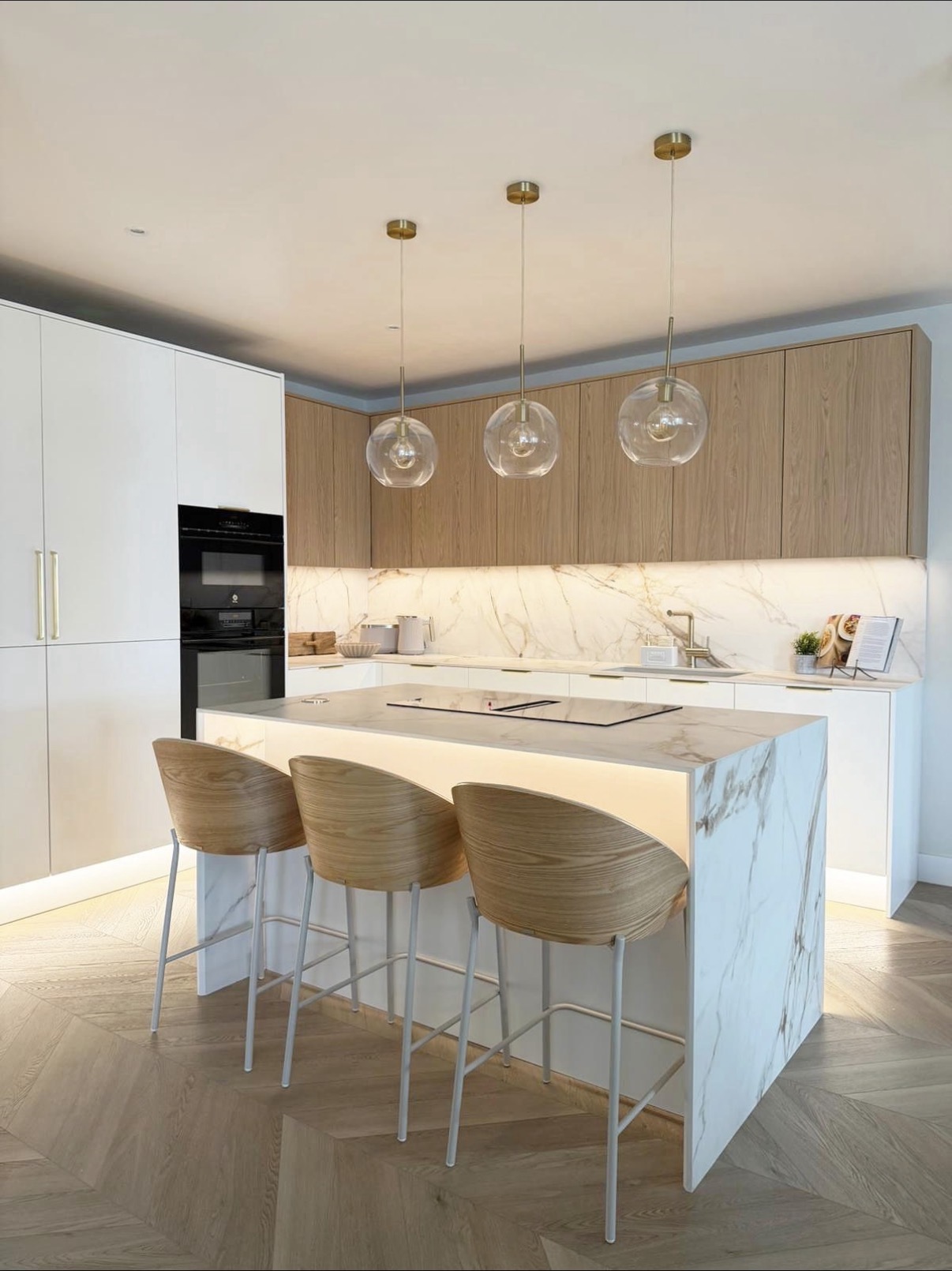 Light oak kitchen with marble island, glass globe pendant lights and sculpted timber bar stools