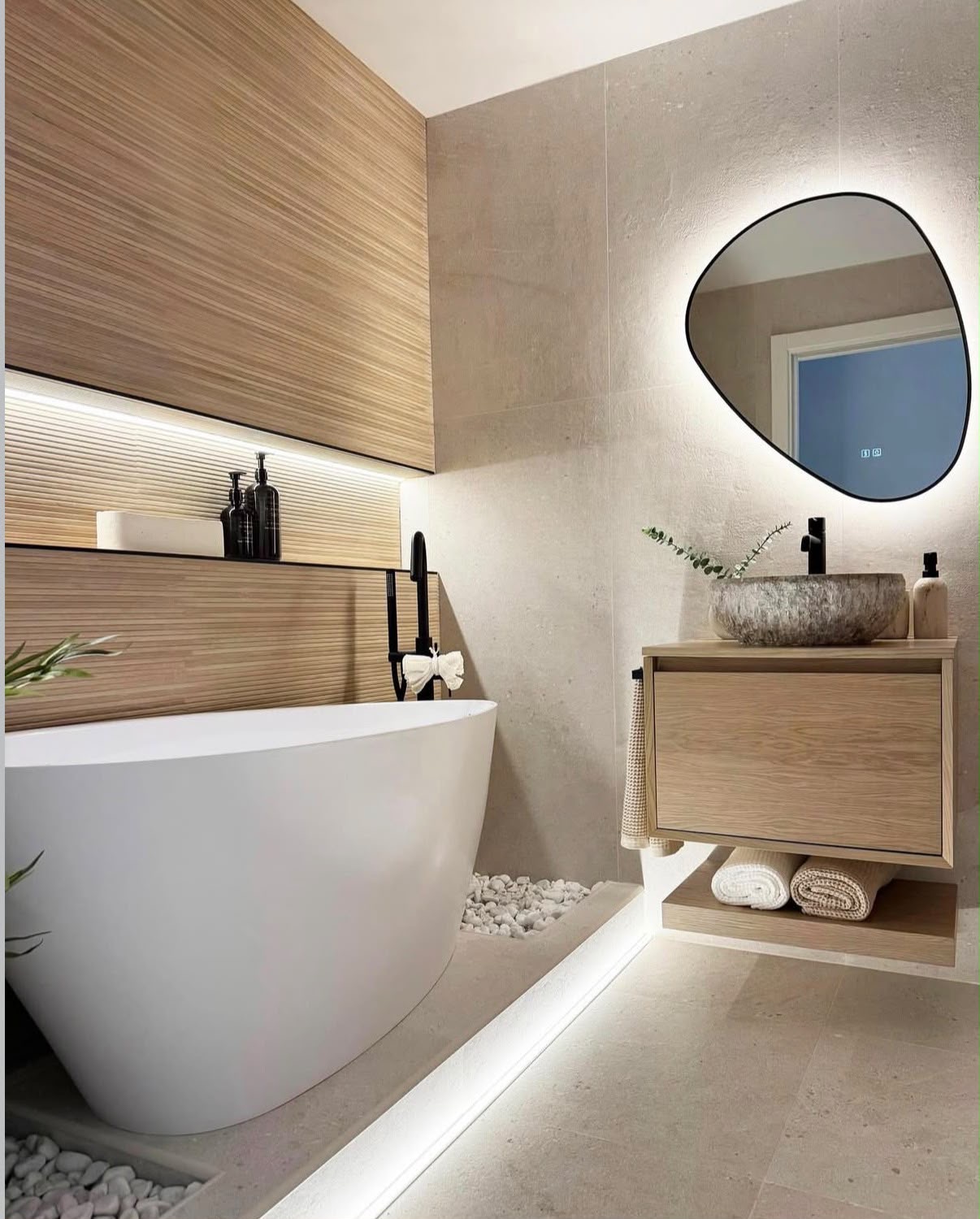 Spa bathroom with a freestanding tub, ribbed timber wall, pebble detailing and a backlit pebble mirror