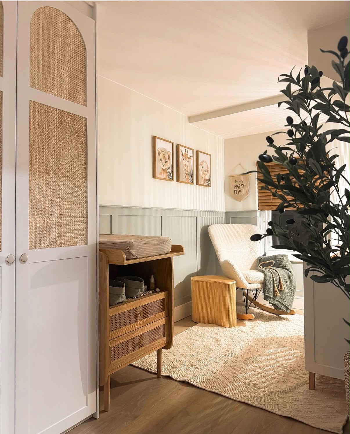 Nursery with sage panelling, rattan wardrobes, oak changing table and bouclé rocking chair