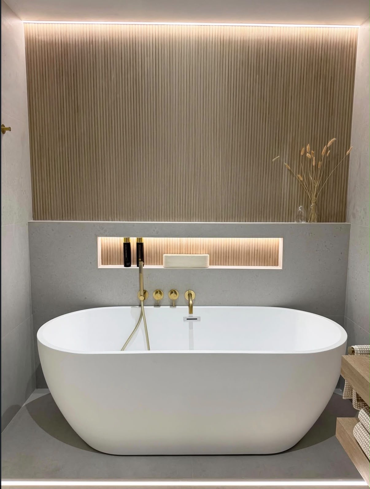 Freestanding bath against a fluted timber feature wall with a lit niche and brushed brass fittings