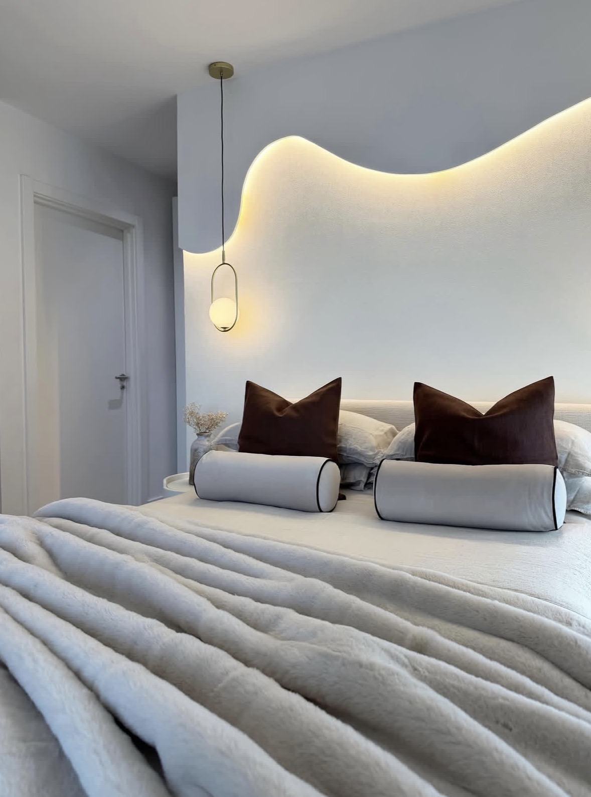 Serene bedroom with a sculptural backlit headboard, ivory bedding and chocolate velvet cushions