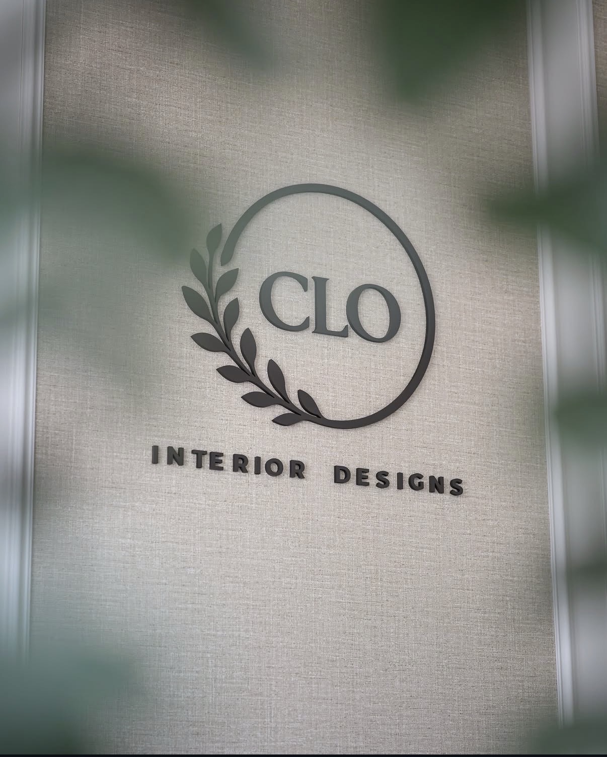 Close-up of the Clo Interior Designs logo mounted on a warm linen-textured wall