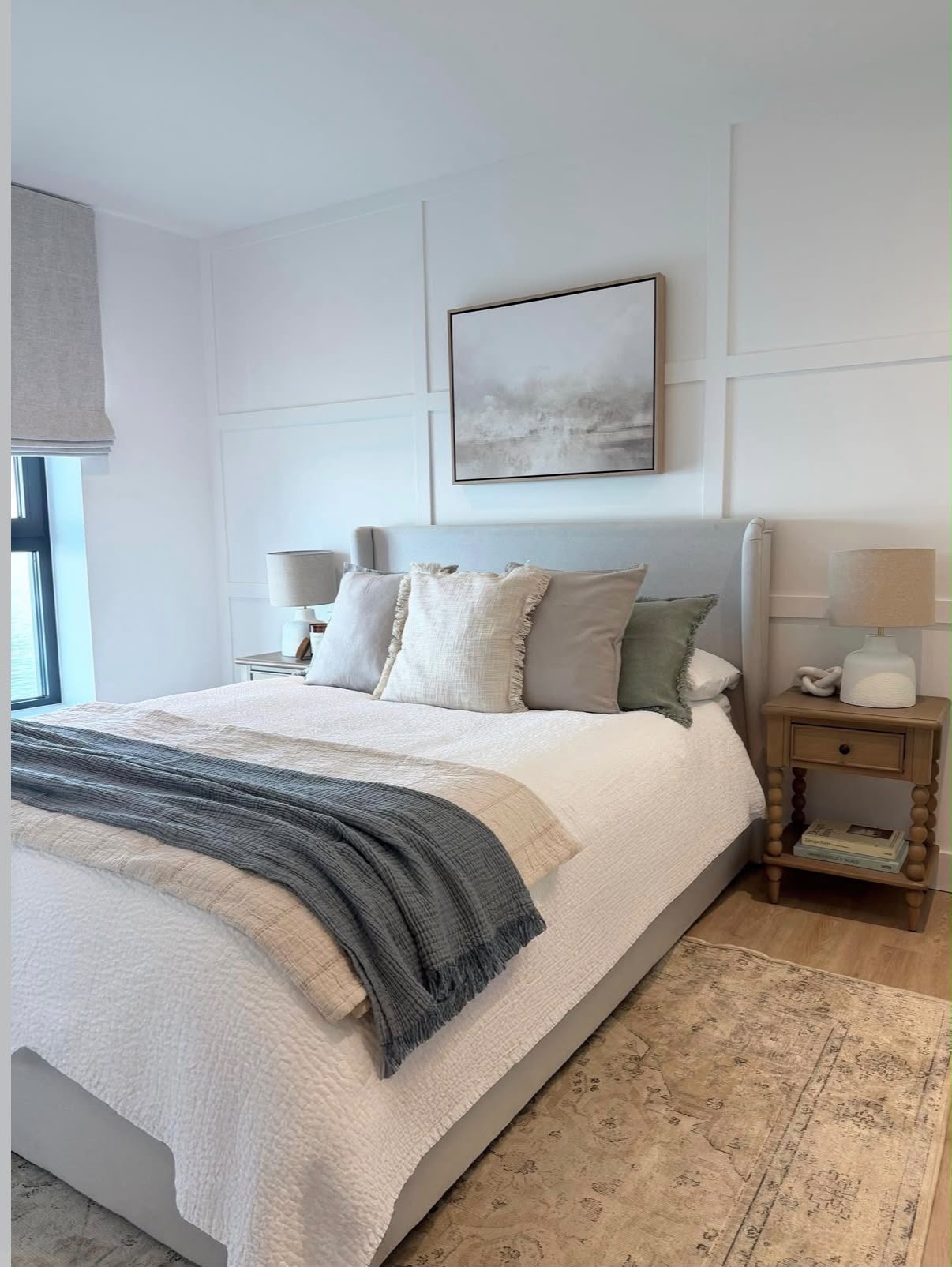 Bright bedroom with panelled wall, soft grey upholstered bed, layered linens and oak bobbin bedside tables